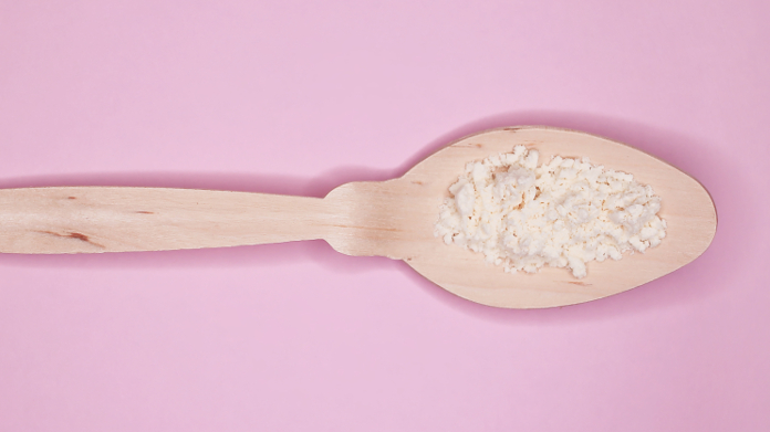 A spoonful of powdered colostrum on a pink background