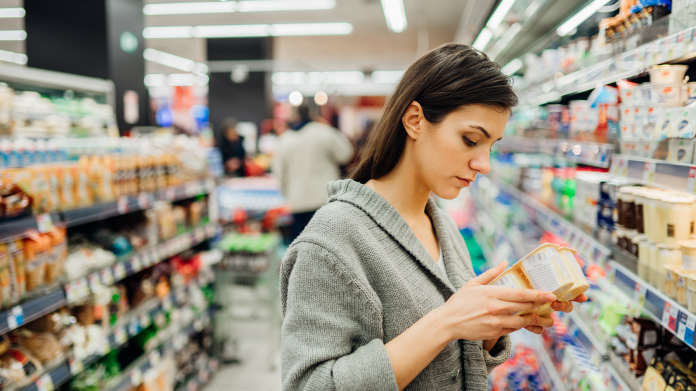 Bleke vrouw die voedingswaarde van een product in de winkel leest