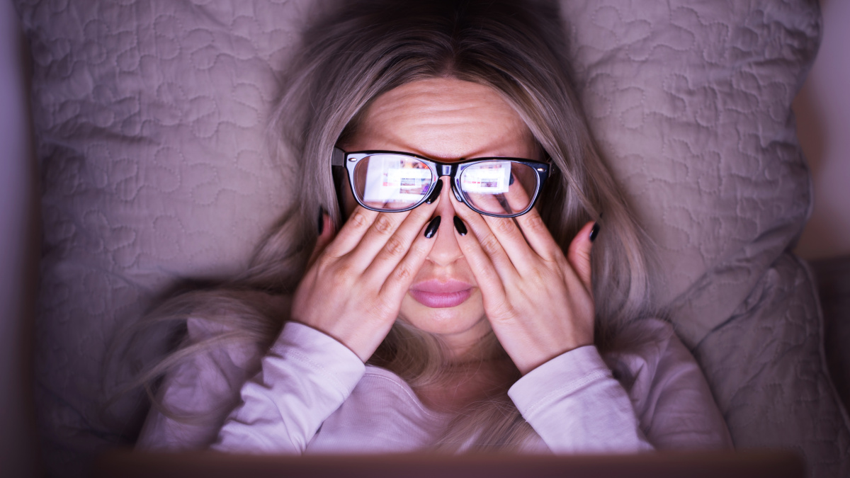 Woman wearing glasses, rubbing her eyes in front of her screen